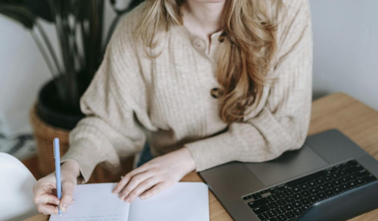 Focused businesswoman writing in notebook near laptop