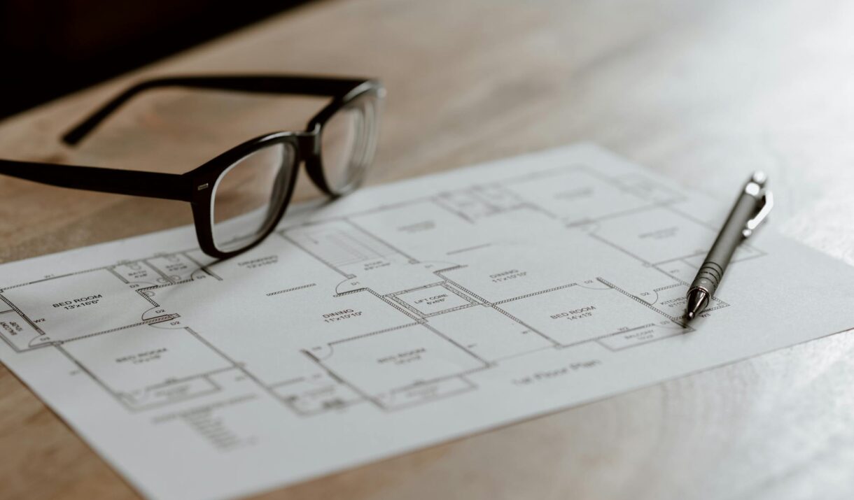 From above of eyeglasses near pen on plan placed on wooden table in apartment in soft daylight